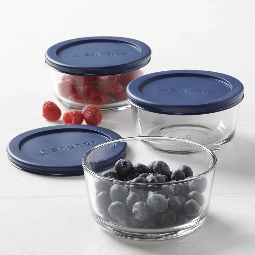 Round glass food storage containers with blue lids, some filled with blueberries and raspberries
