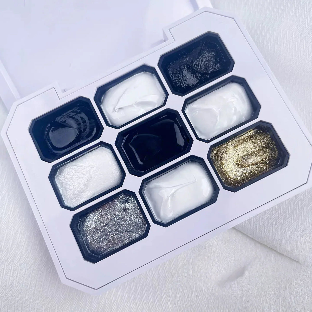 A nine-color solid gel nail polish palette with various black, white, and metallic shades in a white case.