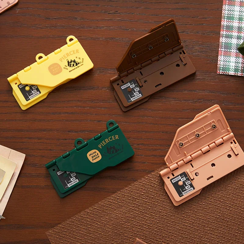 A flat lay of four different colored portable mini hole punchers on a wooden table.