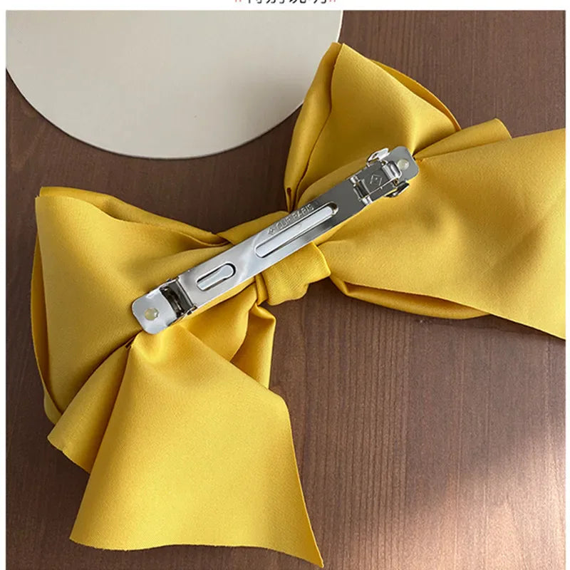 A yellow satin bow hair clip showing the metal fastener on the back