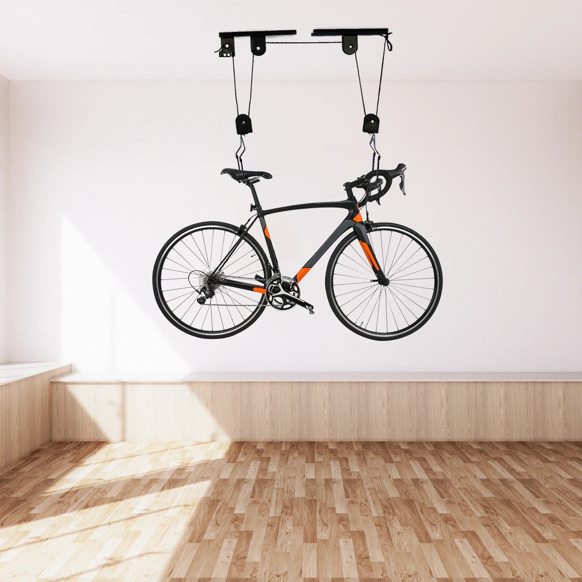A black road bike hanging from the ceiling via a wall-mounted pulley hoist system.