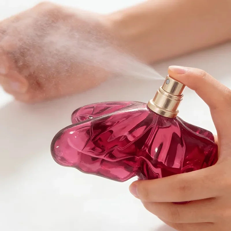 A person spraying a pink butterfly-shaped glass perfume bottle into the air.