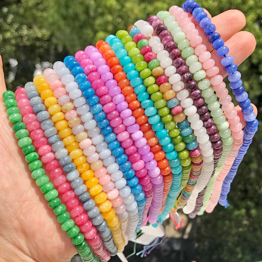 Close up of hand holding rows of assorted colorful natural stone rondelle beads