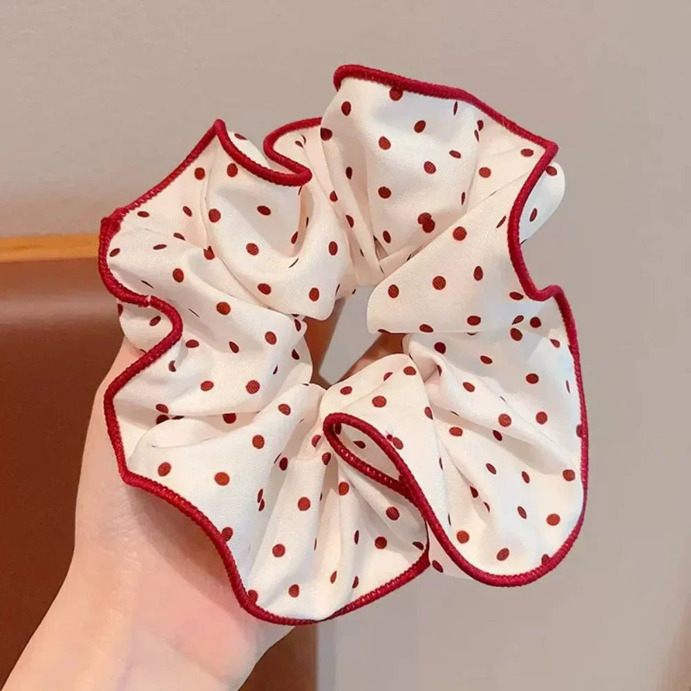 A white hair scrunchie with red polka dots and a ruffled red trim being held in a hand