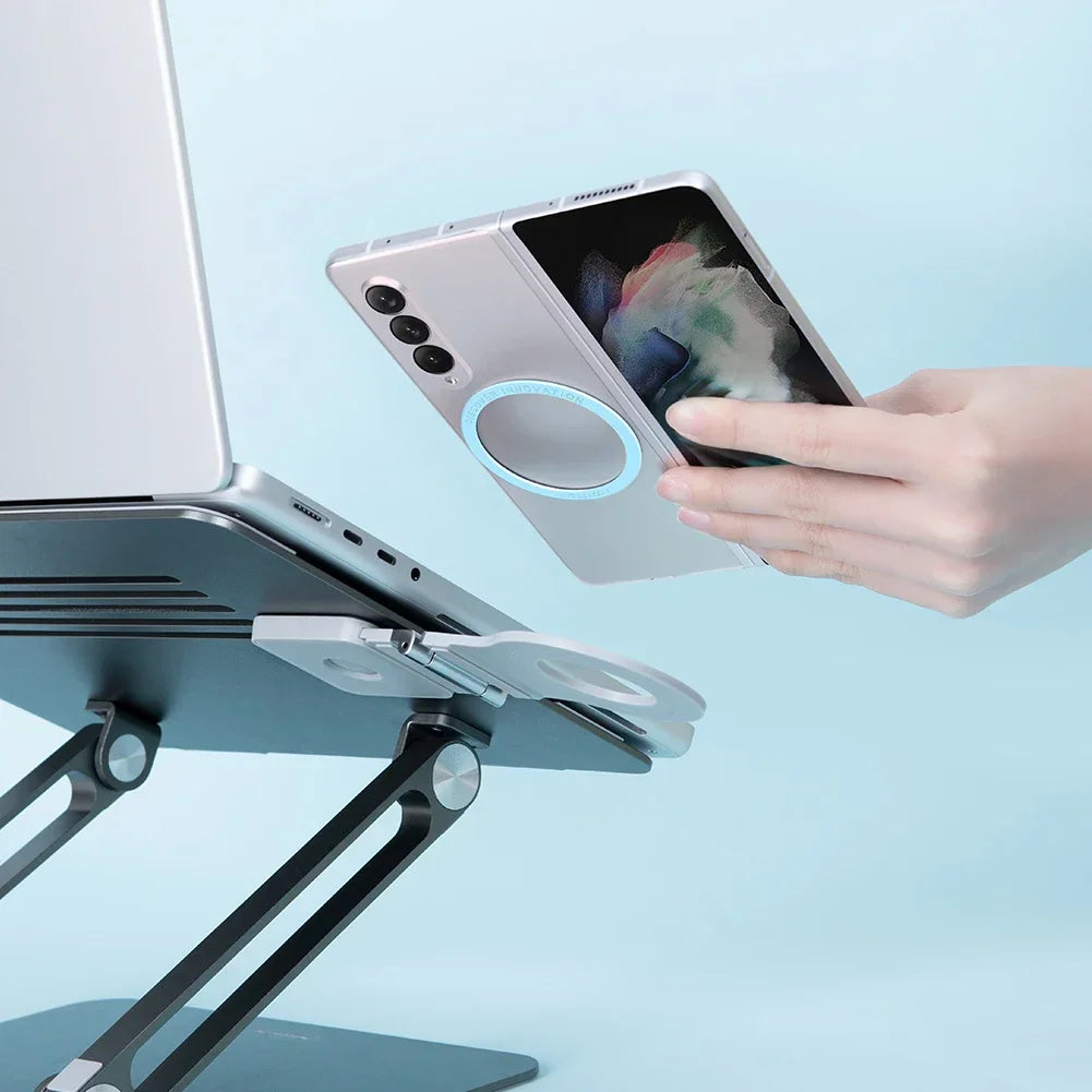 Person holding a smartphone with an attached magnetic ring near a laptop stand