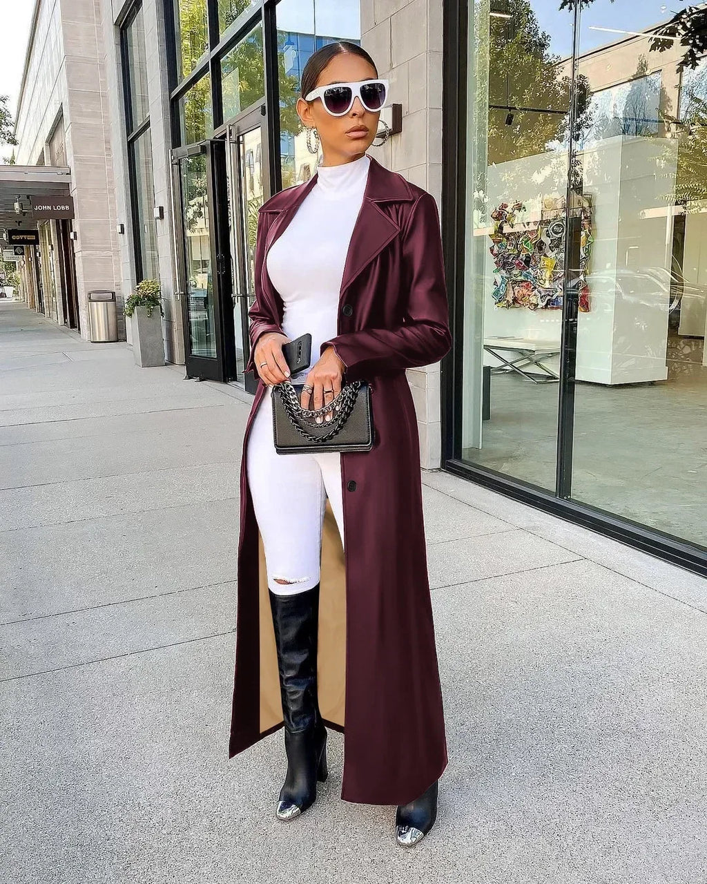 A woman wearing a maroon leather trench coat over a white top and pants.