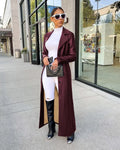 A woman wearing a maroon leather trench coat over a white top and pants.