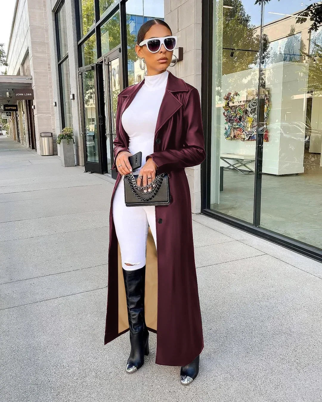 A woman wearing a maroon leather trench coat over a white top and pants.