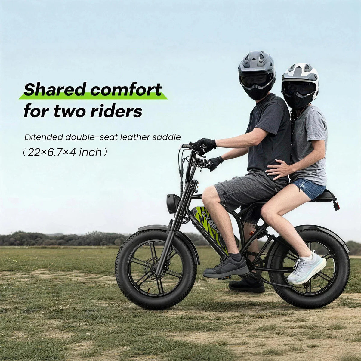 Two people wearing helmets riding a black fat tire electric bike on a field.