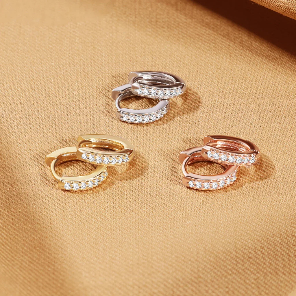 Three pairs of small hoop earrings in silver, gold and rose gold with small crystals placed on a textured fabric.