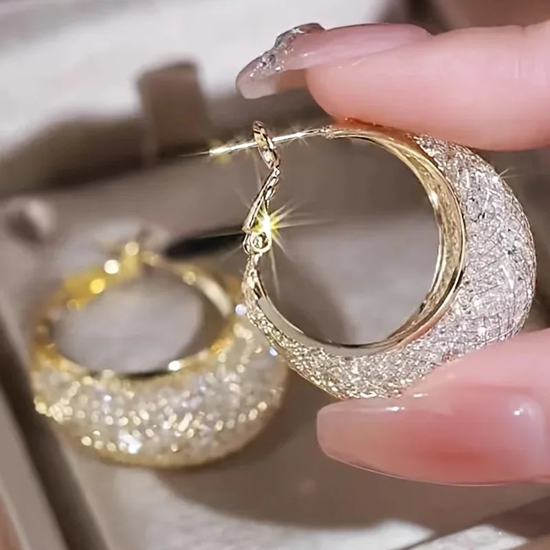 Close-up of sparkling textured gold-tone hoop earrings held in hand