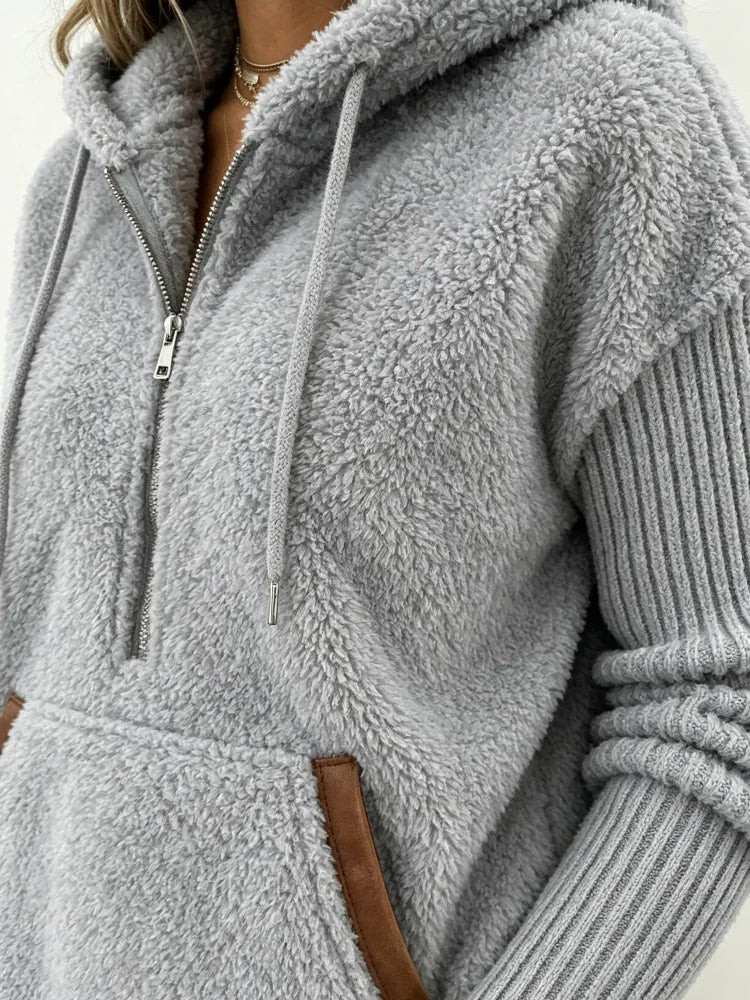 Close-up of the front of the gray fuzzy fleece hoodie showing the hood, drawstrings, zipper, and pocket detail.