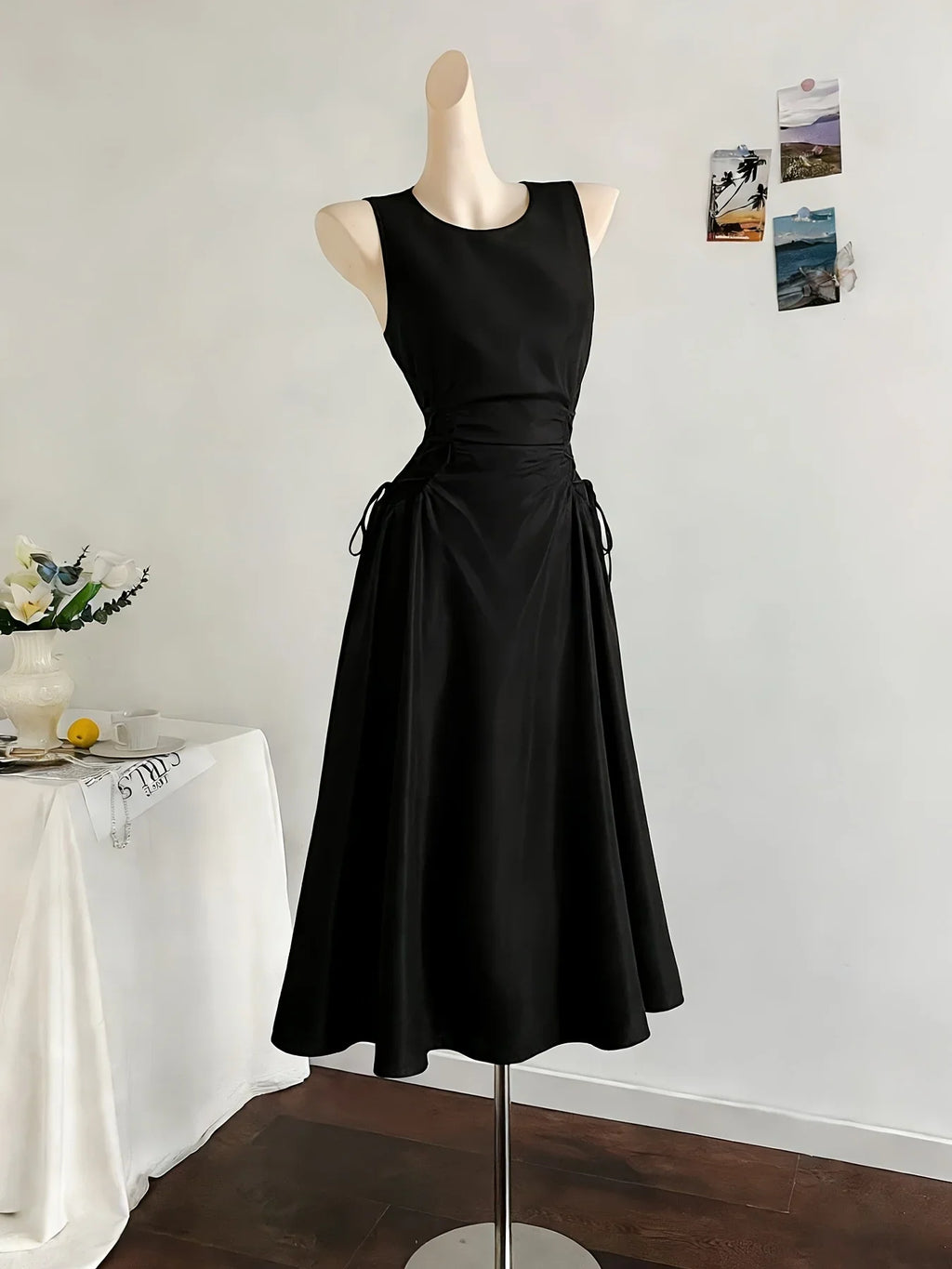 A black sleeveless midi dress with side waist ties displayed on a mannequin.