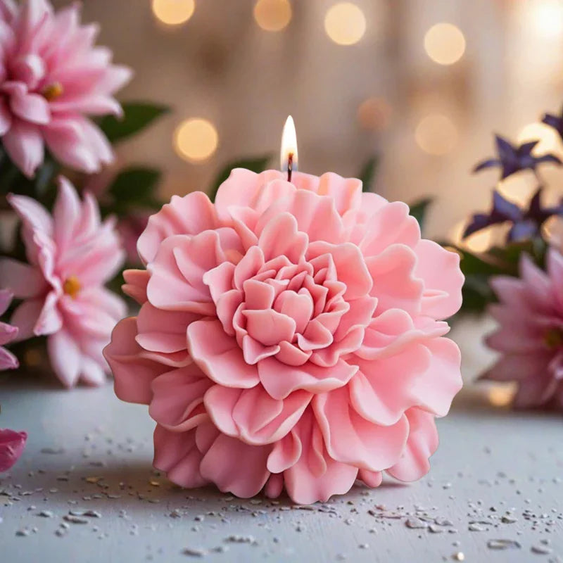 A pink peony shaped flower candle with a burning wick