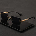Rimless rectangular sunglasses with black lenses and gold panther-style metal temples on a black display base