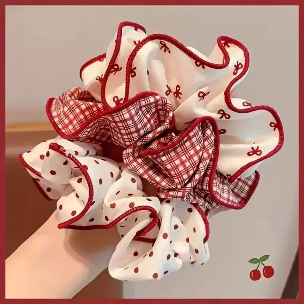 A red and white plaid hair scrunchie being held in a hand with a decorative cherry icon in the corner