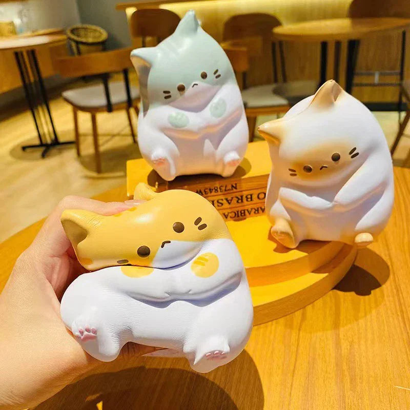 Three different colored cat-shaped stress relief toys sitting on a yellow surface.