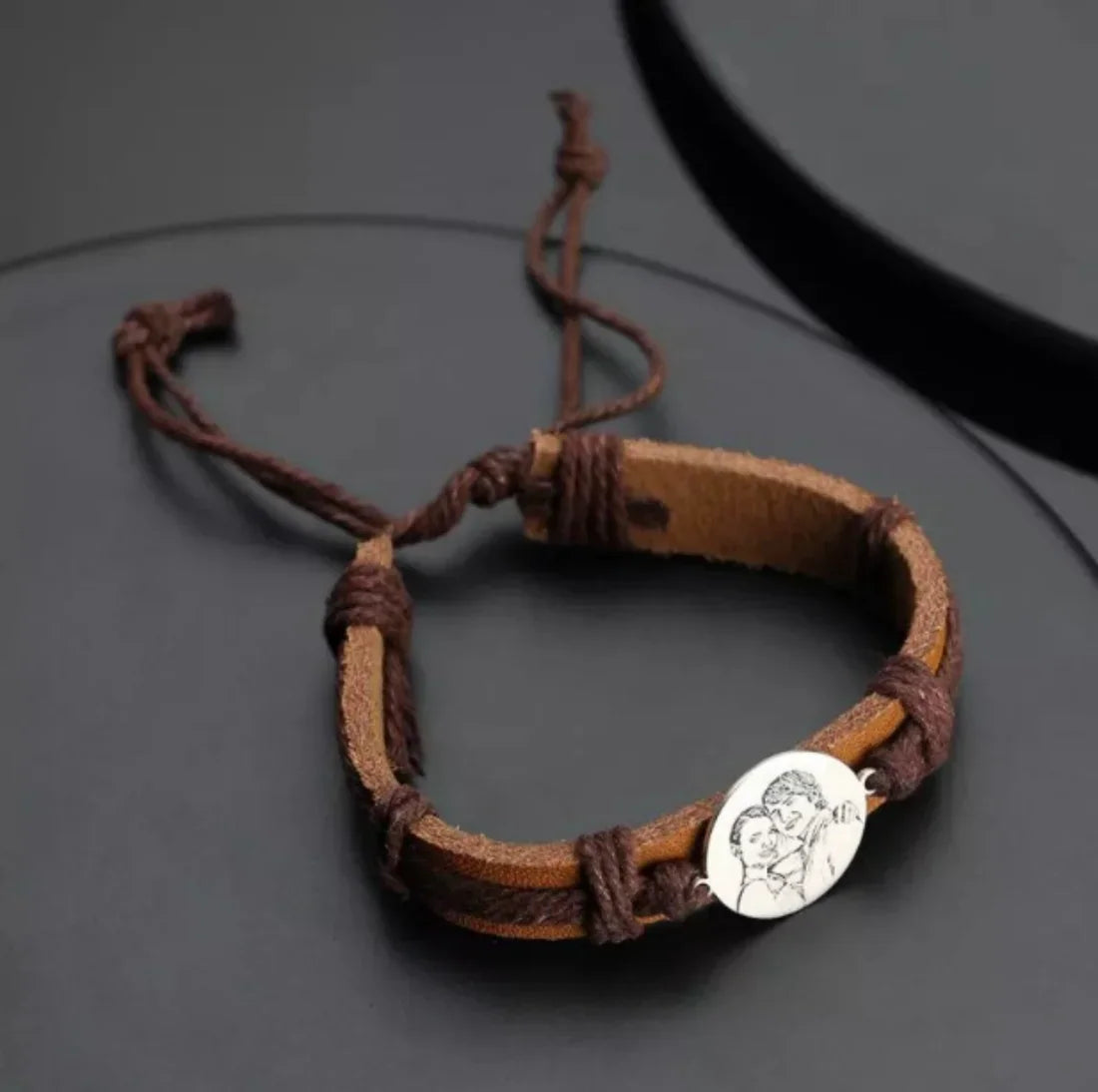 Close up of a brown leather braided bracelet with a metal round charm engraved with a portrait.