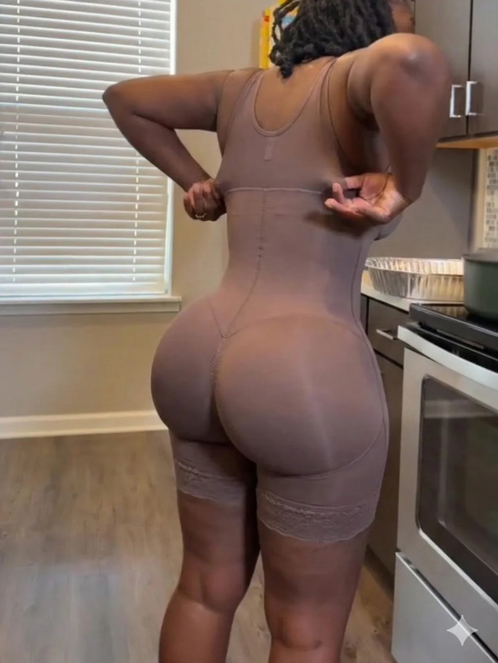 A woman wearing a brown full body shapewear bodysuit with lace details on the thighs.