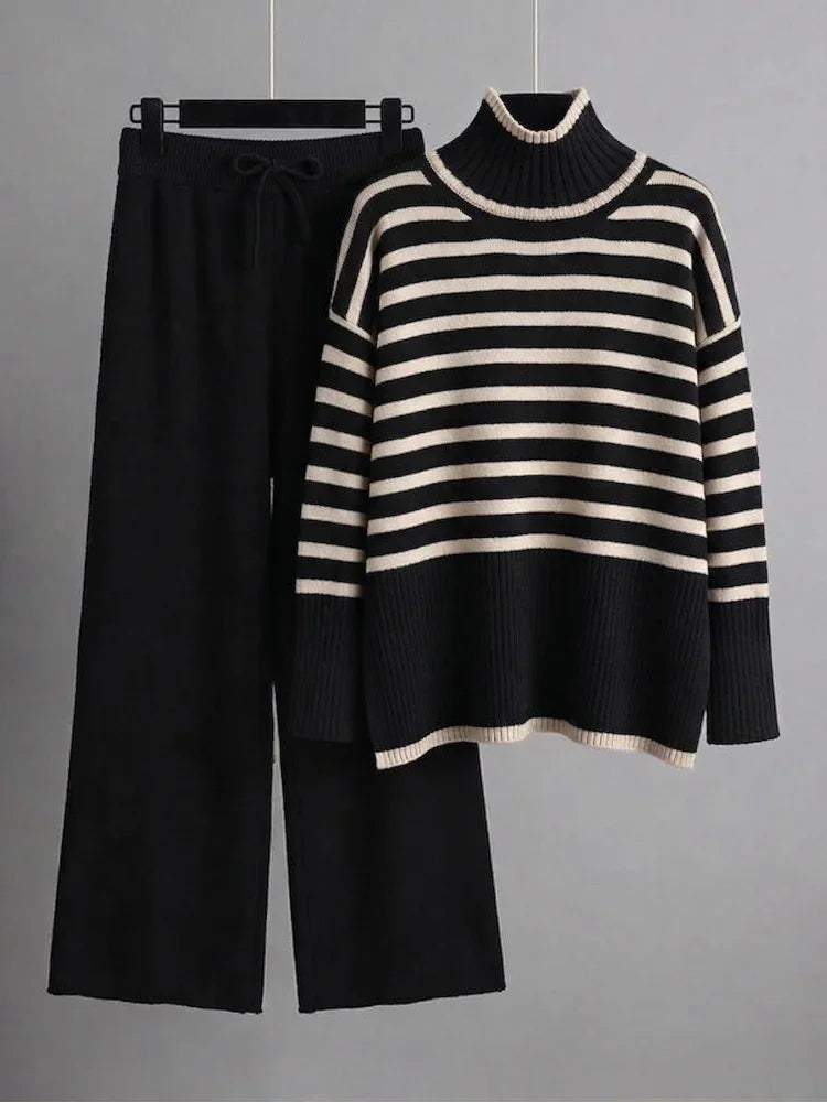 Set consisting of black knit wide leg pants and a black and white striped high neck sweater hanging on a hanger