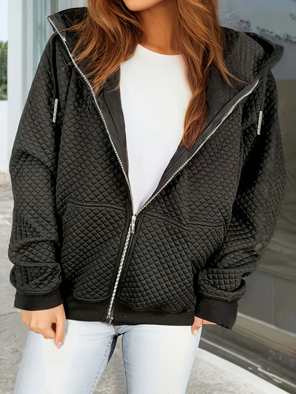 A black diamond-quilted zip-up hooded jacket with ribbed cuffs, worn over a white shirt and blue jeans.