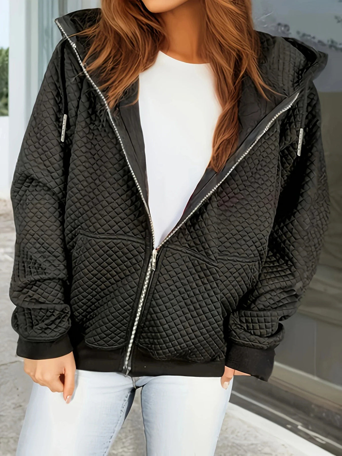 A black diamond-quilted zip-up hooded jacket with ribbed cuffs, worn over a white shirt and blue jeans.