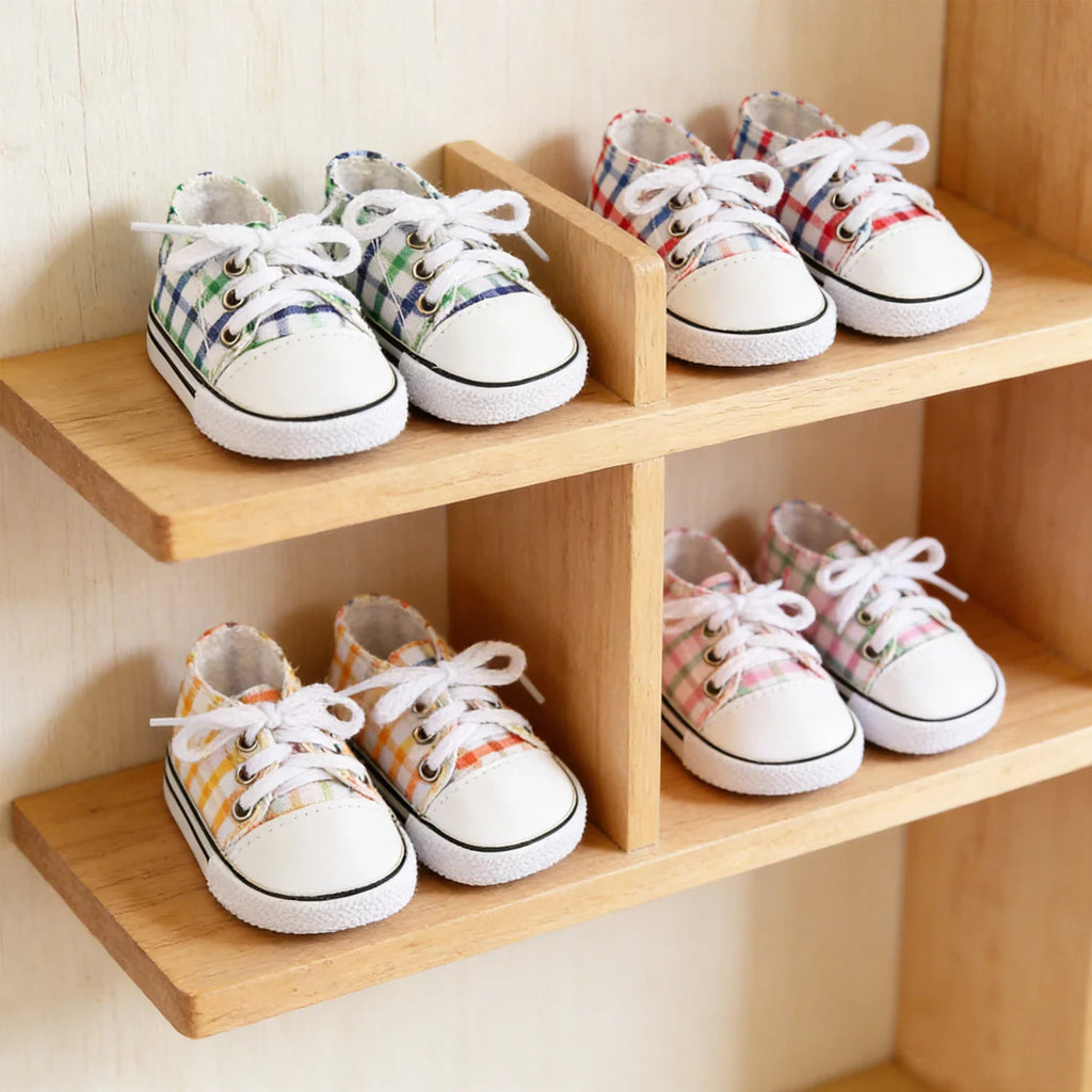 Four pairs of colorful checkered canvas doll shoes with white laces and toes, displayed on a wooden shelf.