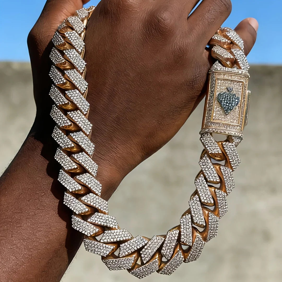 Hand holding gold cuban link chain with spade emblem clasp against blue sky