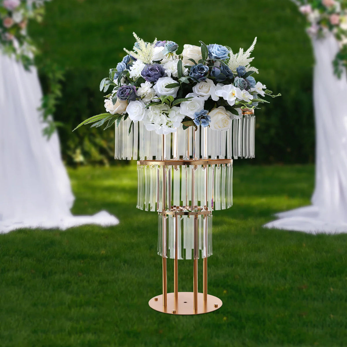 Three-tier gold metal wedding centerpiece stand decorated with flowers and hanging crystal prisms.