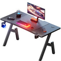 Black carbon fiber gaming desk with accessories, headphones, and monitor