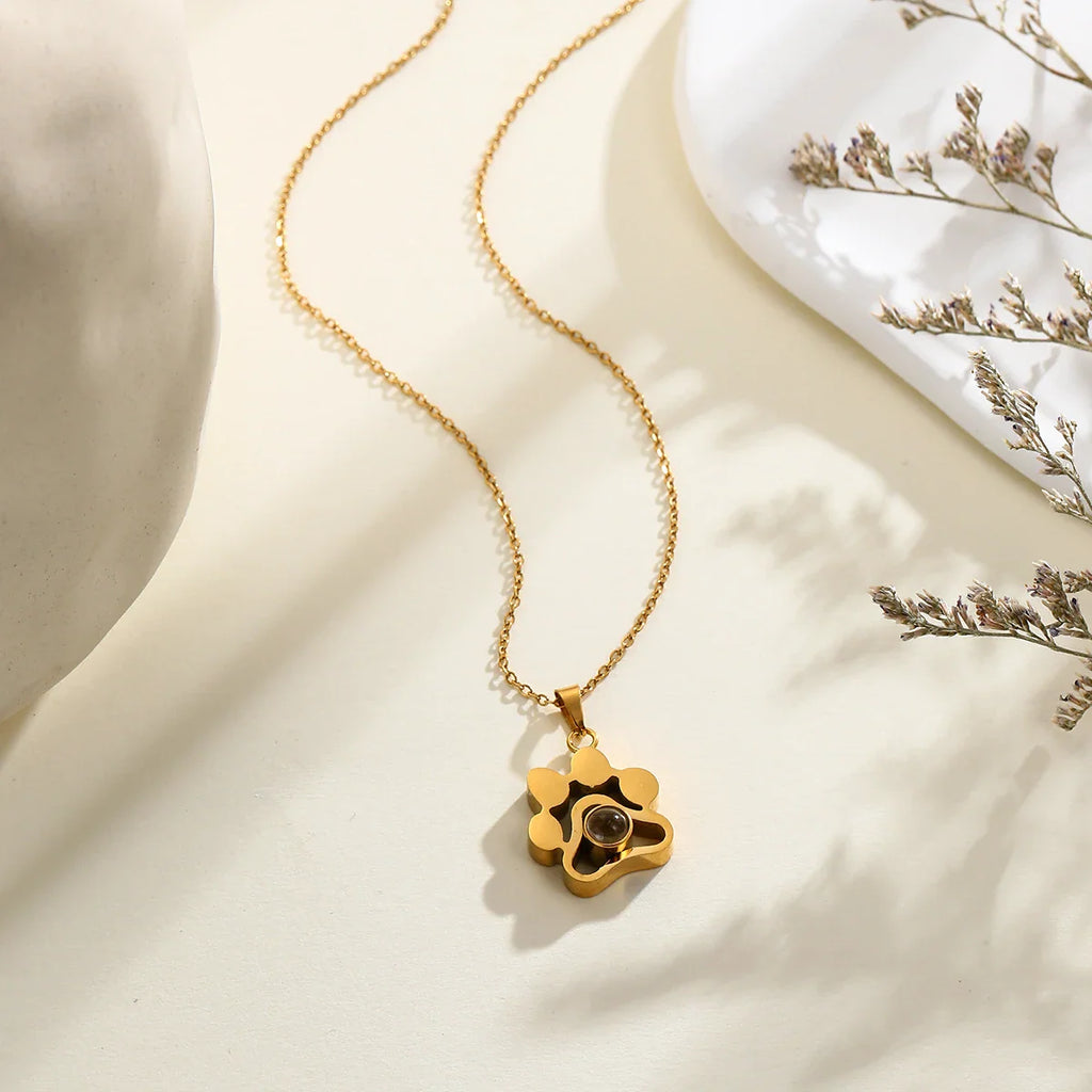 Gold paw-shaped projection necklace on a neutral surface.