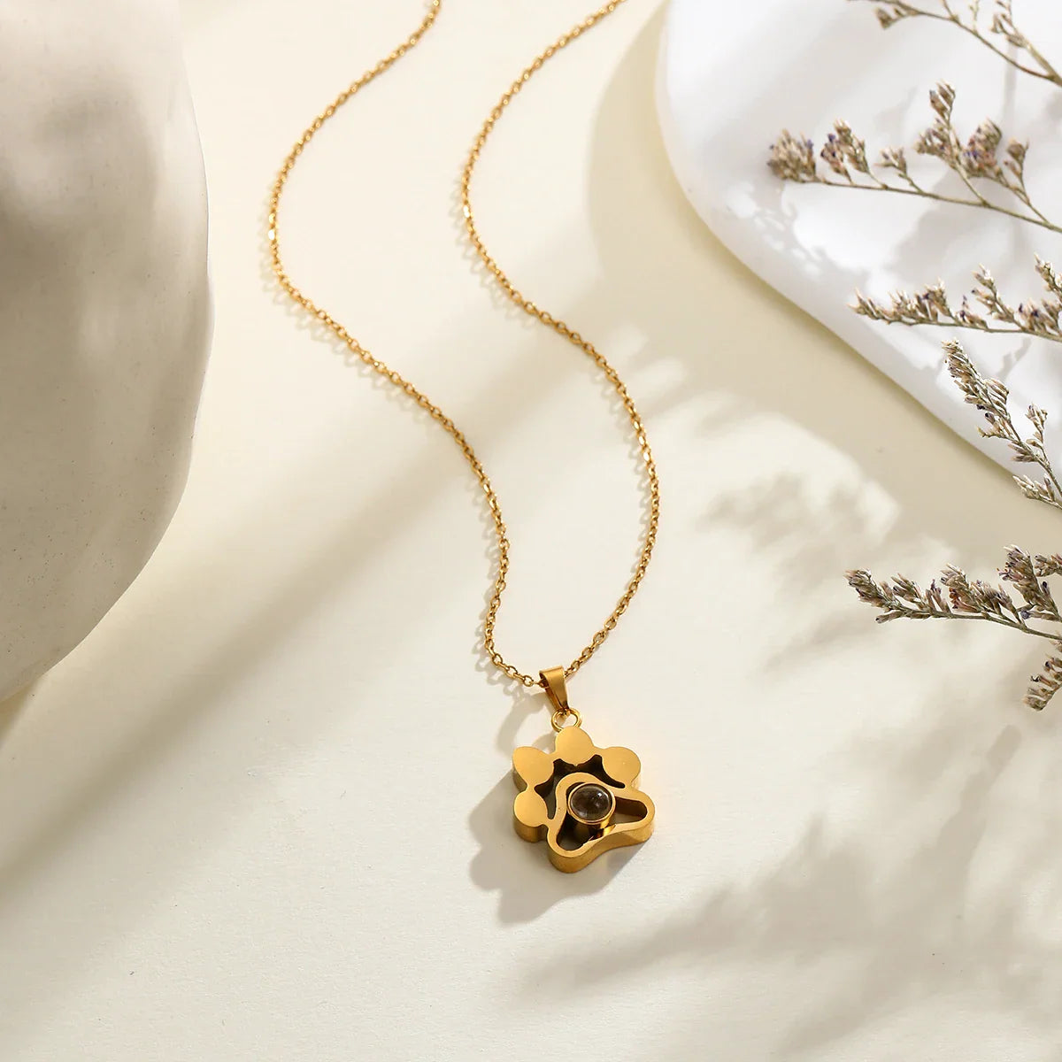 Gold paw-shaped projection necklace on a neutral surface.