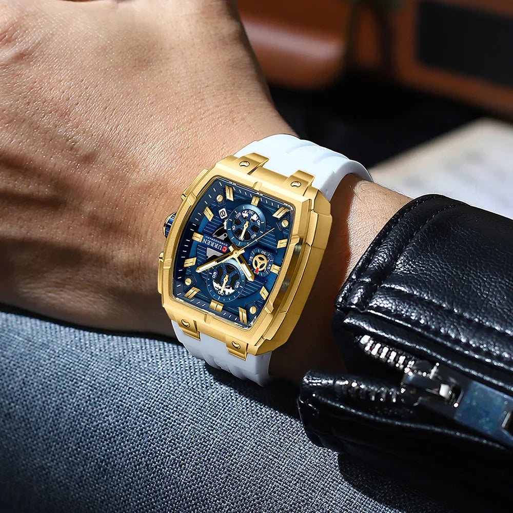 Men's square chronograph watch with gold case, blue dial, and white silicone strap worn on wrist