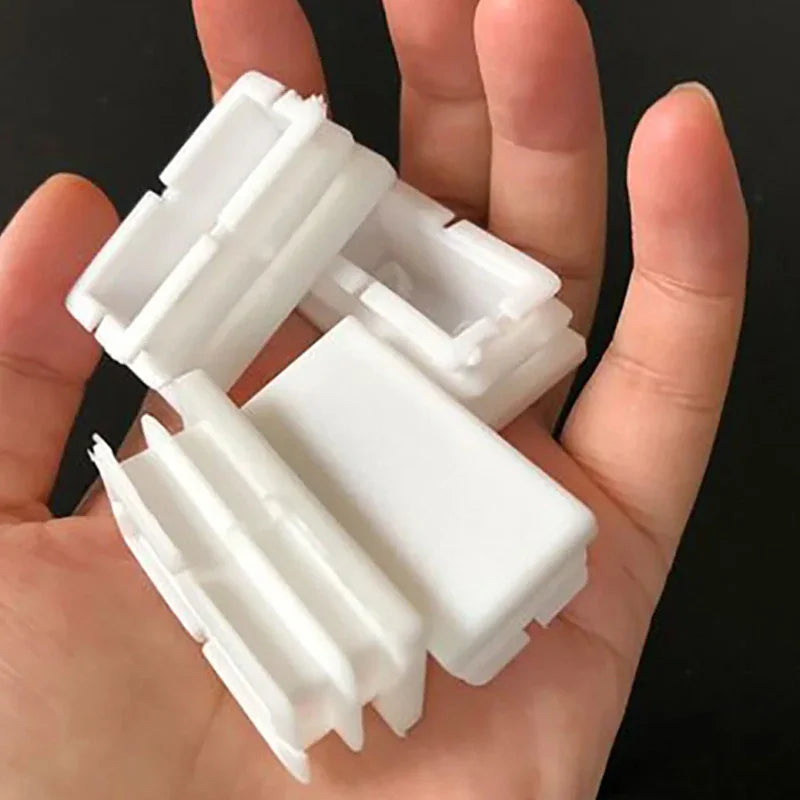 Several white plastic rectangular tube end caps held in a hand