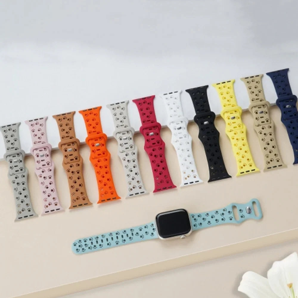 Assorted colors of silicone watch bands with paw print cutouts laid out on a surface