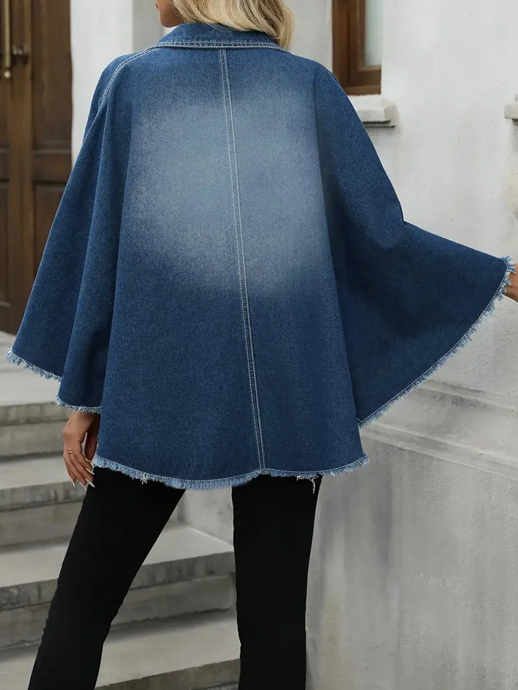 The back view of a plus-size blue denim jacket with a faded wash and frayed hem