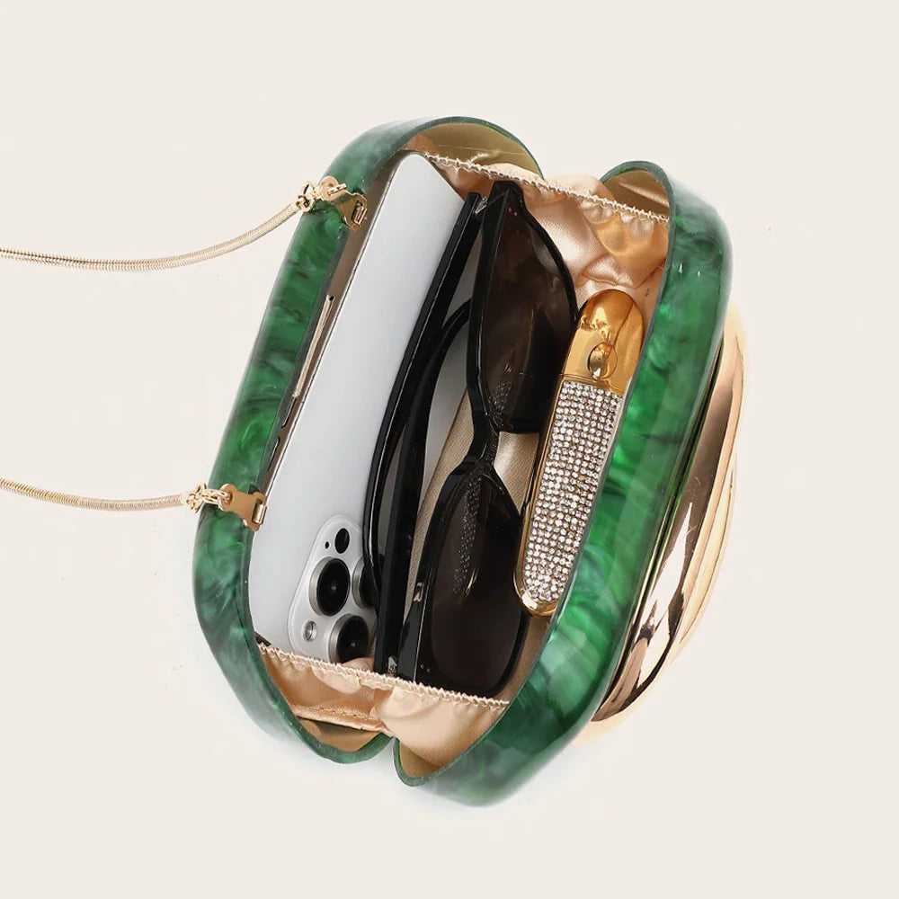 Top view of an open green marble-effect evening clutch containing a phone, sunglasses, and a sparkling lipstick.