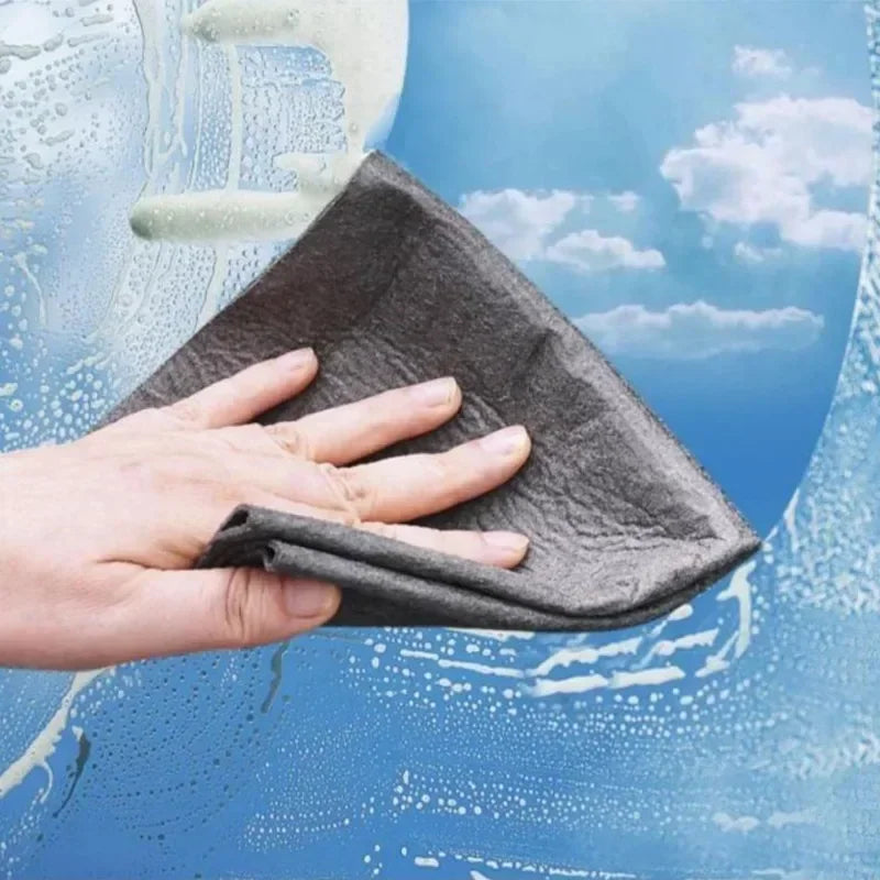 A hand using a grey microfiber cloth to clean a soapy window.