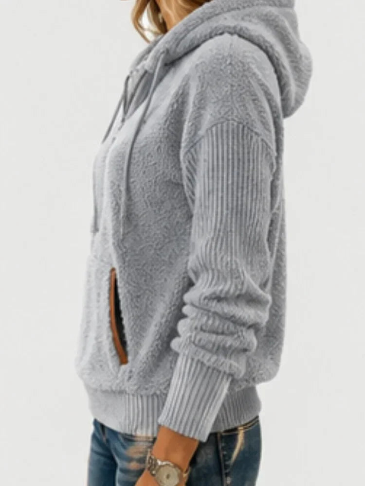 A side view of a woman wearing a gray fuzzy fleece half-zip hoodie with ribbed sleeves.