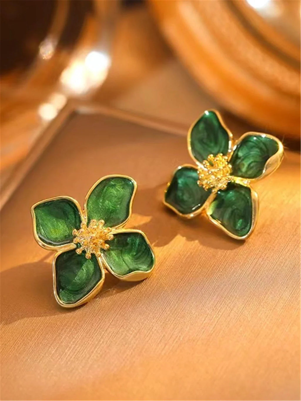 Green floral stud earrings on a gold textured background