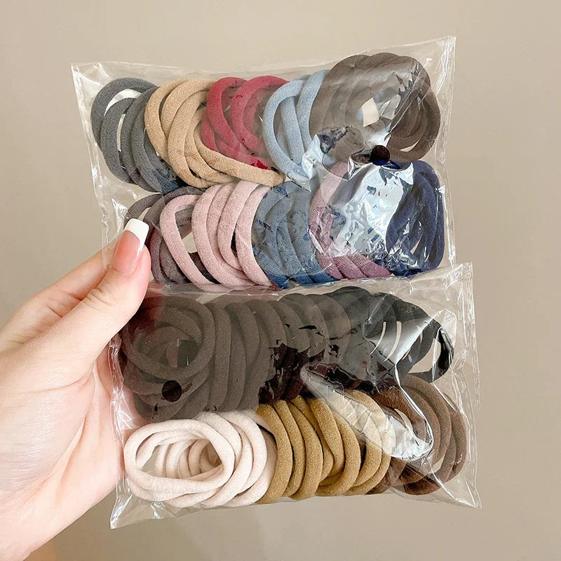 Hand holding a transparent plastic bag containing a collection of brown, tan, and blue nylon hair ties.