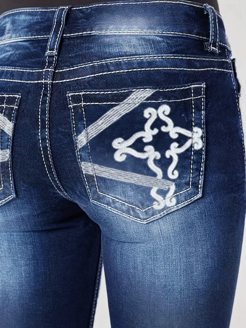 Close up of back pocket on deep blue jeans with white decorative stitching and embroidery