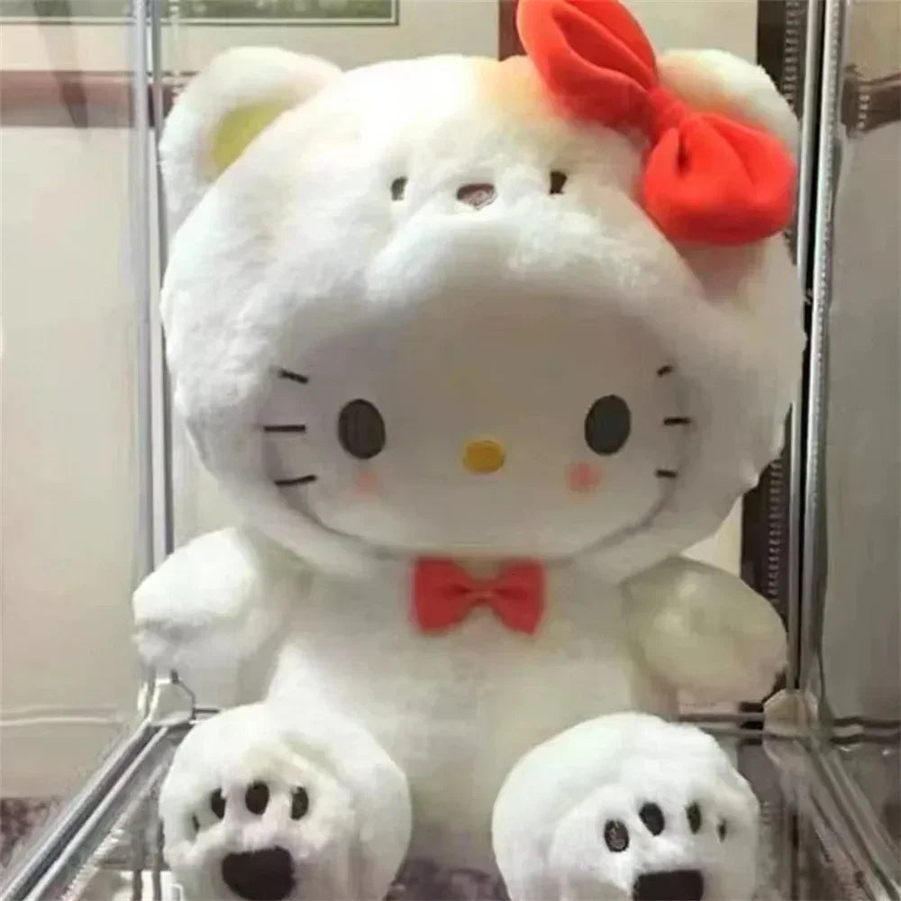 A white plush cat toy with a red bow and bear hood sitting in a display case.