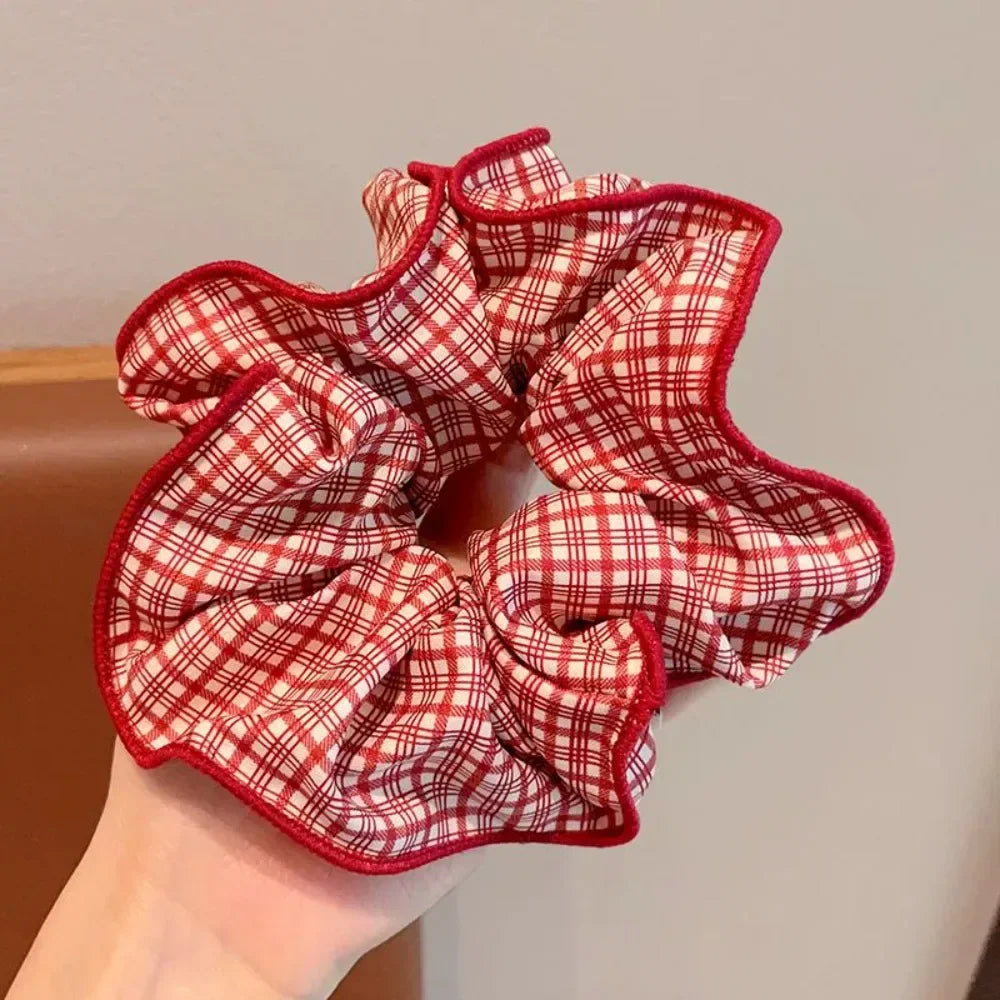 A red and white plaid hair scrunchie with a ruffled red trim being held in a hand