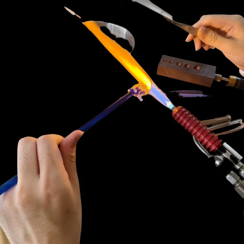 Artisan using a torch to shape a piece of blue glass.