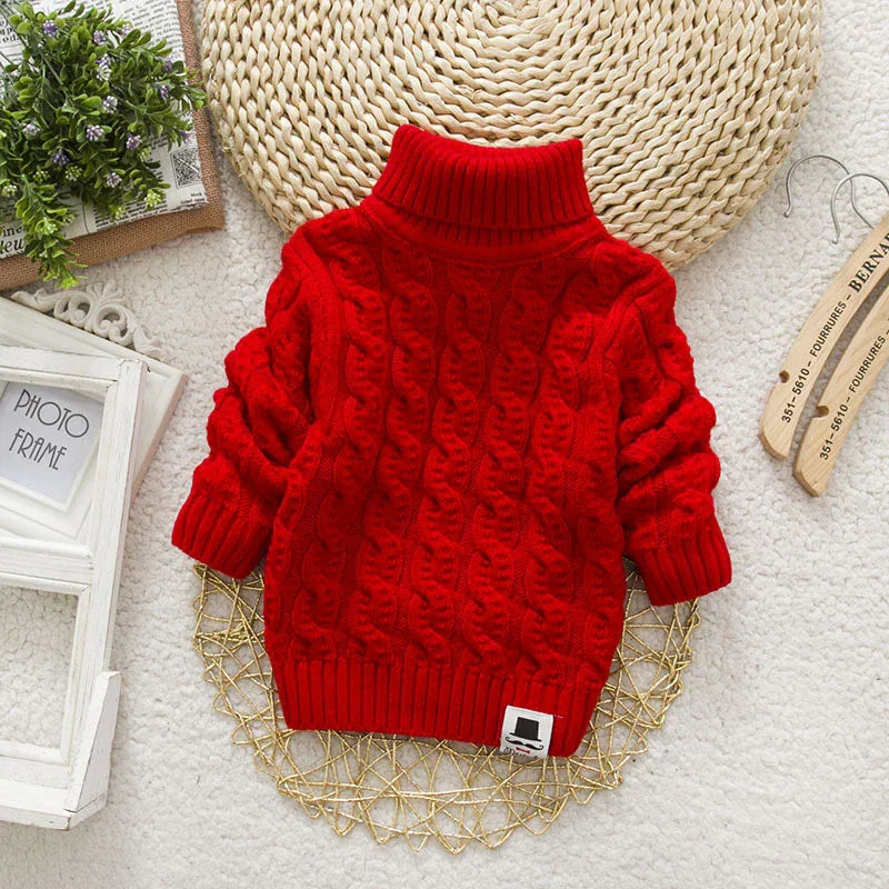A red cable-knit turtleneck sweater laid flat with a mustache logo patch.