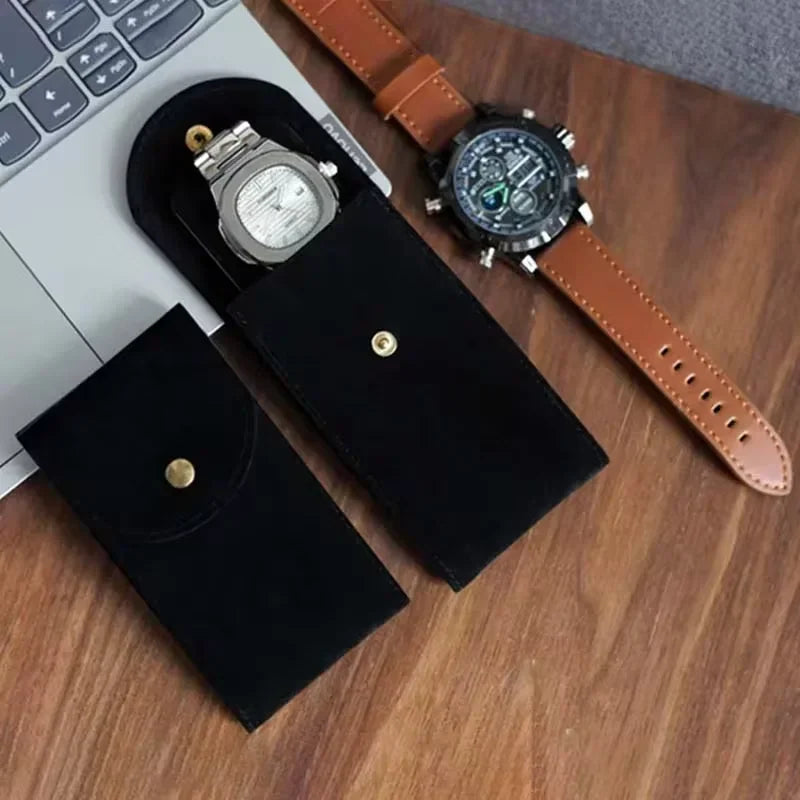 Black suede watch storage pouches on a wooden table next to a laptop.