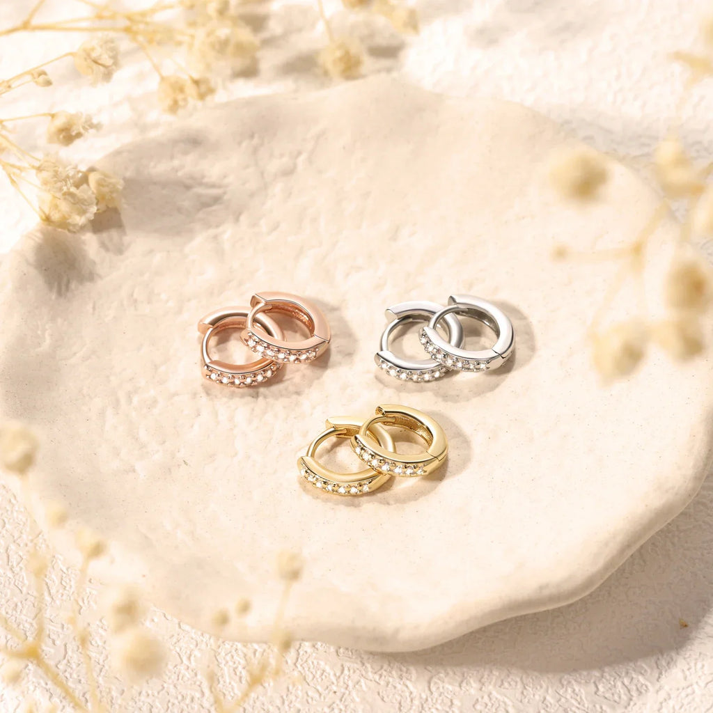 Three pairs of small crystal hoop earrings in silver, gold and rose gold placed on a small ceramic dish.