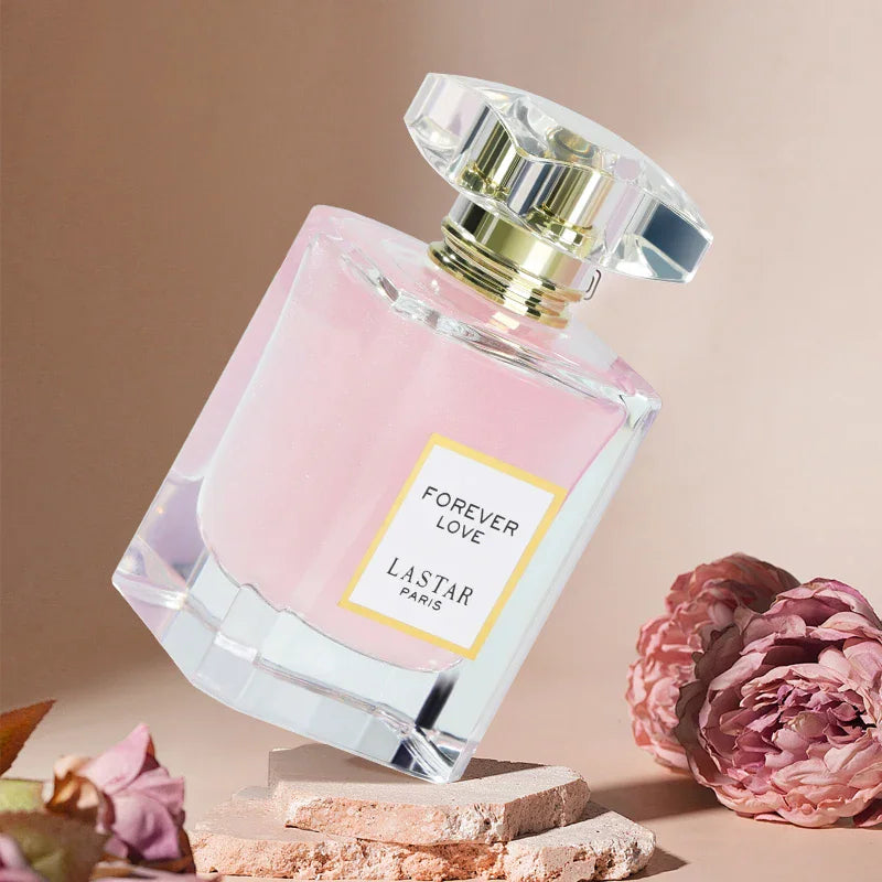 Pink perfume bottle resting on stone pieces with pink flowers in the background