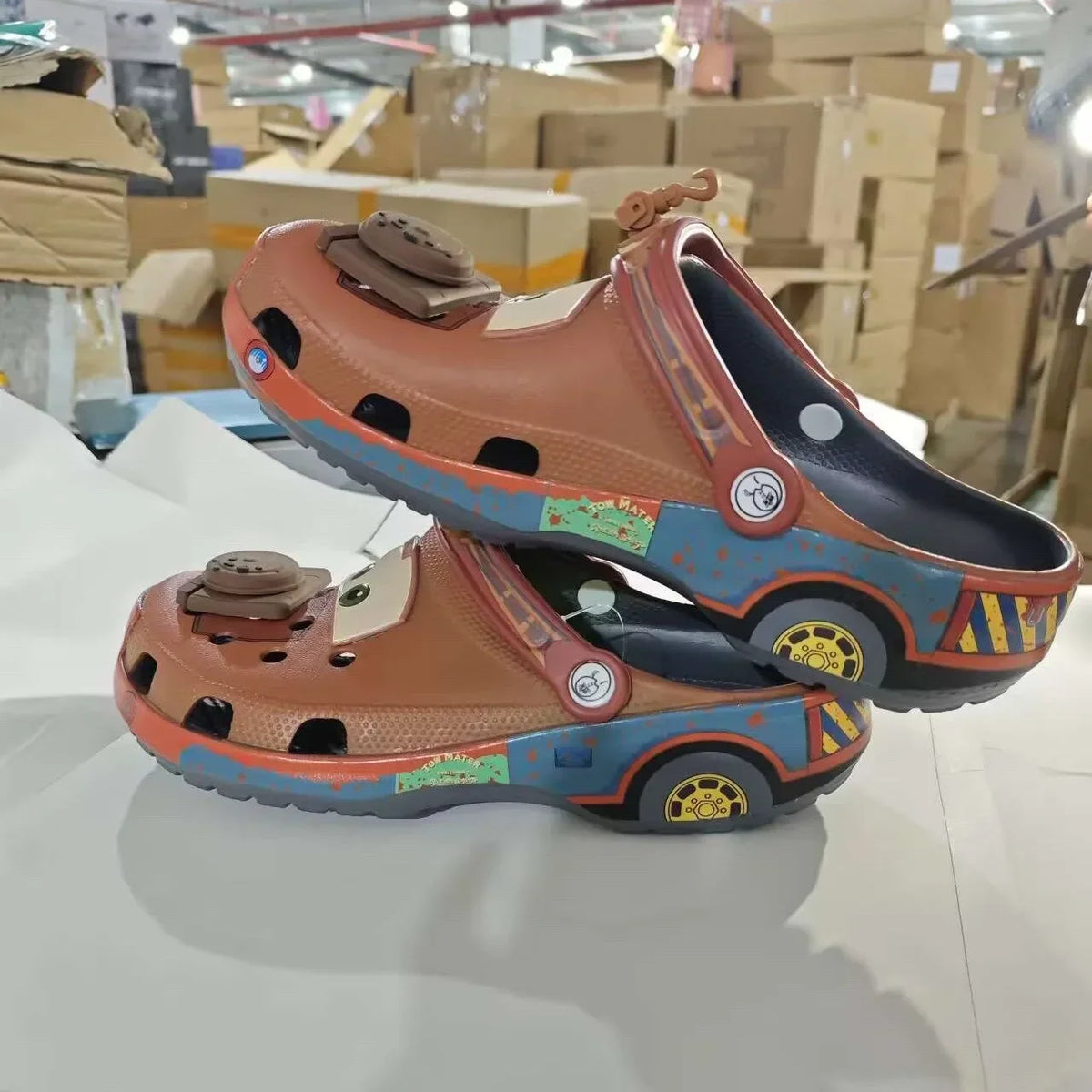 Side profile of brown cartoon tow truck themed clogs featuring wheel graphics and weathered detailing.